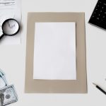 Vista superior de calculadora, caneta e materiais financeiros sobre uma mesa, com uma folha em branco.