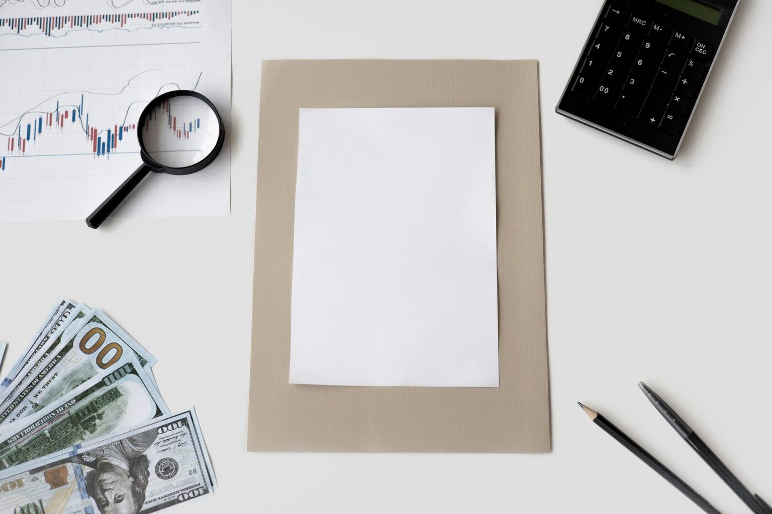 Vista superior de calculadora, caneta e materiais financeiros sobre uma mesa, com uma folha em branco.
