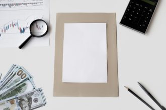 Vista superior de calculadora, caneta e materiais financeiros sobre uma mesa, com uma folha em branco.