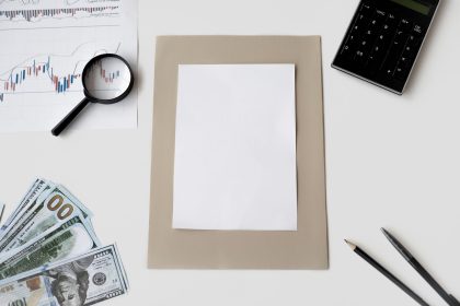 Vista superior de calculadora, caneta e materiais financeiros sobre uma mesa, com uma folha em branco.
