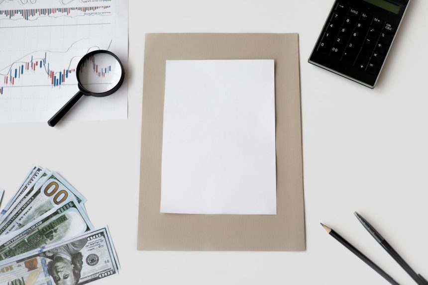 Vista superior de calculadora, caneta e materiais financeiros sobre uma mesa, com uma folha em branco.