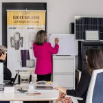 Equipe em reunião analisa soluções de energia solar diante de painéis e quadro branco em um escritório.