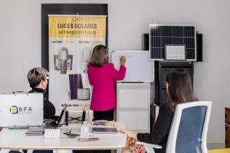 Equipe em reunião analisa soluções de energia solar diante de painéis e quadro branco em um escritório.