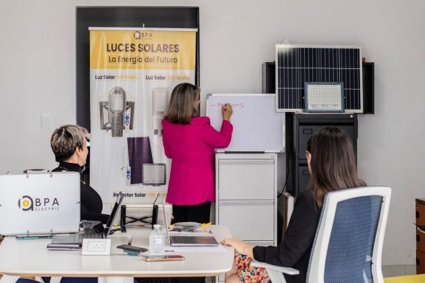 Equipe em reunião analisa soluções de energia solar diante de painéis e quadro branco em um escritório.