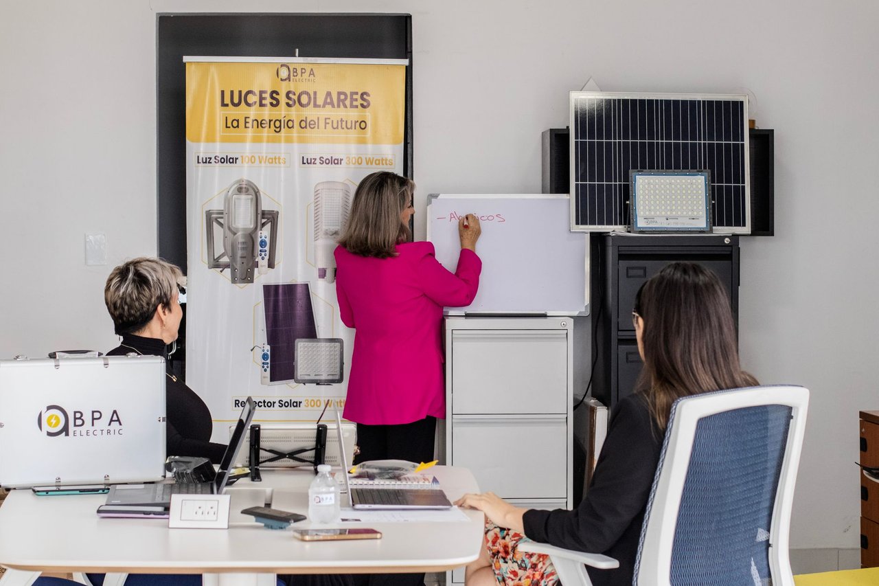 Equipe em reunião analisa soluções de energia solar diante de painéis e quadro branco em um escritório.